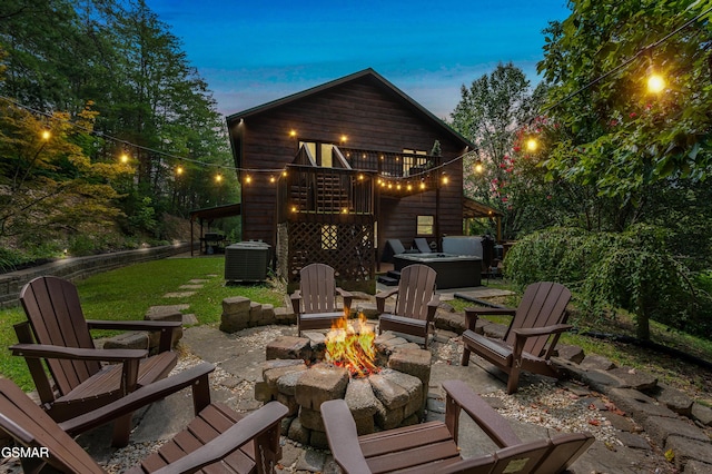 patio terrace at dusk featuring a yard, a balcony, a fire pit, and central AC unit