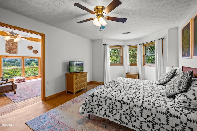 bedroom with ceiling fan, light hardwood / wood-style floors, and a textured ceiling