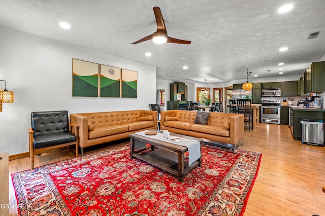 living room featuring a textured ceiling, light hardwood / wood-style floors, and ceiling fan