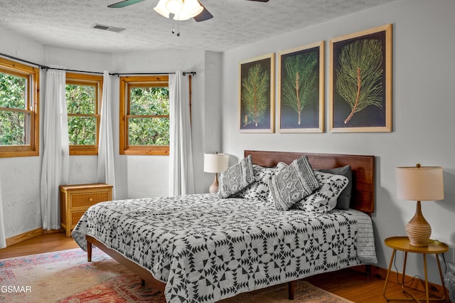 bedroom with hardwood / wood-style floors, ceiling fan, and a textured ceiling