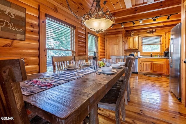 dining area with rail lighting, light hardwood / wood-style flooring, log walls, and sink