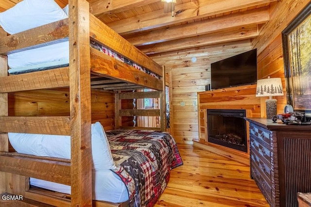 bedroom with wood walls, beam ceiling, light wood-type flooring, and wood ceiling