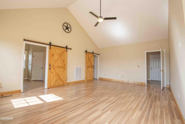 interior space with light wood finished floors, high vaulted ceiling, a barn door, and visible vents