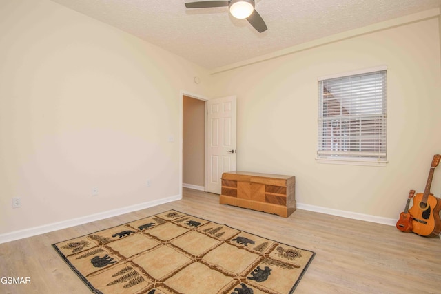 interior space with ceiling fan, a textured ceiling, baseboards, and wood finished floors