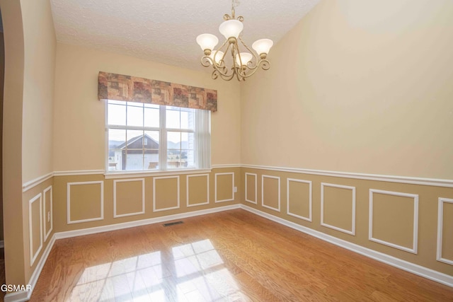 unfurnished room featuring visible vents, wood finished floors, a textured ceiling, a decorative wall, and a notable chandelier