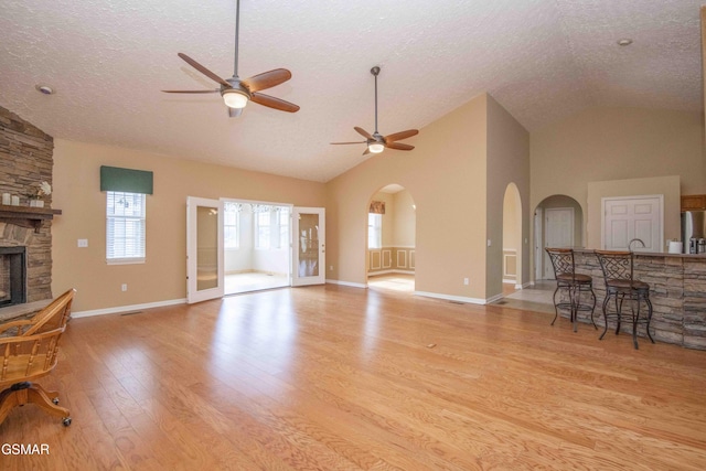 living area with a textured ceiling, ceiling fan, arched walkways, light wood-style flooring, and a fireplace