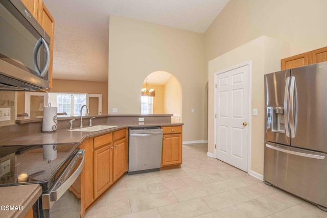 kitchen featuring arched walkways, light tile patterned floors, stainless steel appliances, a peninsula, and a sink