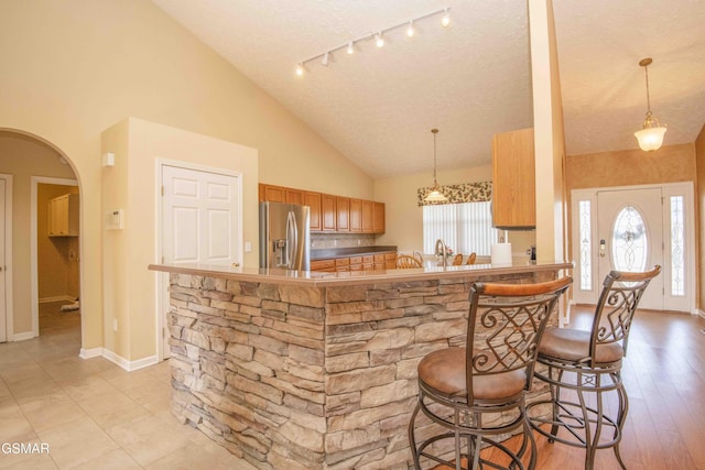 kitchen with arched walkways, brown cabinets, stainless steel refrigerator with ice dispenser, a peninsula, and a kitchen bar