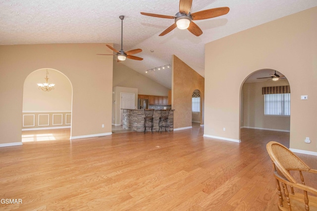 unfurnished living room with arched walkways, high vaulted ceiling, and wood finished floors