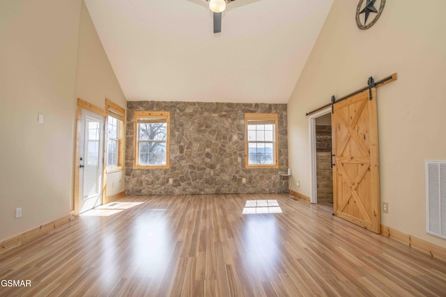 unfurnished living room with high vaulted ceiling, visible vents, light wood-style floors, and a barn door