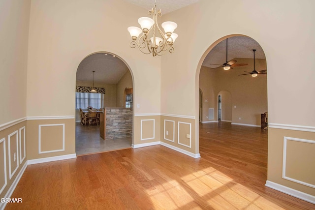 unfurnished room with arched walkways, visible vents, a decorative wall, wood finished floors, and high vaulted ceiling