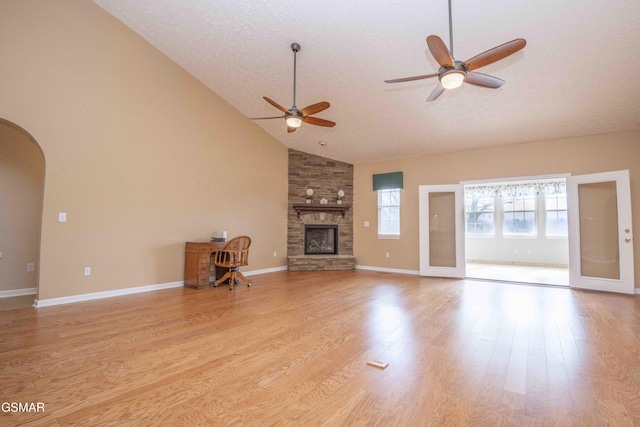 unfurnished living room featuring arched walkways, high vaulted ceiling, a fireplace, baseboards, and light wood-style floors