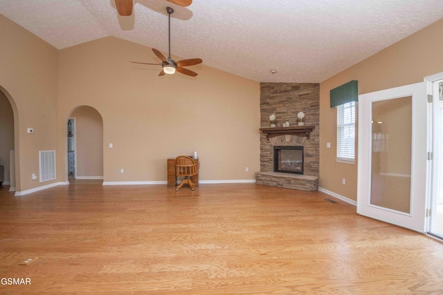 unfurnished living room with arched walkways, a fireplace, visible vents, vaulted ceiling, and light wood finished floors