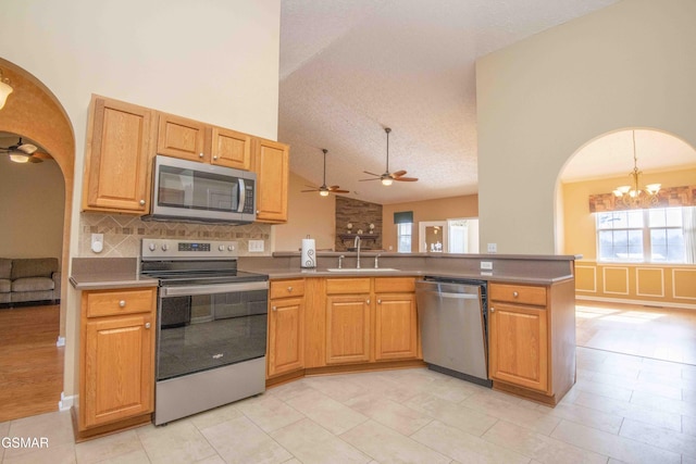 kitchen with arched walkways, decorative backsplash, a peninsula, stainless steel appliances, and a sink