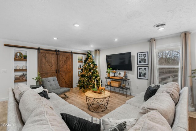 living room featuring a barn door, crown molding, light hardwood / wood-style floors, and a textured ceiling