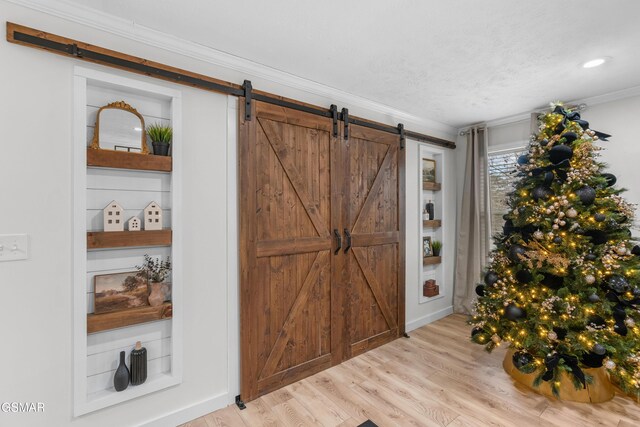 entryway featuring light wood-type flooring, a barn door, and ornamental molding