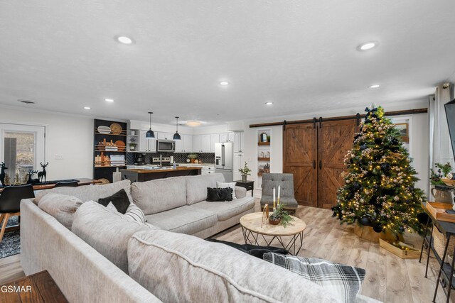 living room with a barn door, sink, light hardwood / wood-style floors, and ornamental molding