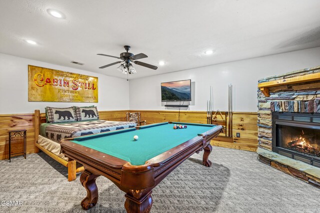 game room with carpet floors, a stone fireplace, ceiling fan, and wooden walls