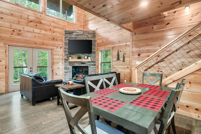 dining space with french doors, wooden walls, hardwood / wood-style flooring, wooden ceiling, and a stone fireplace