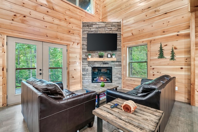 living room featuring a stone fireplace, wooden walls, french doors, and hardwood / wood-style flooring