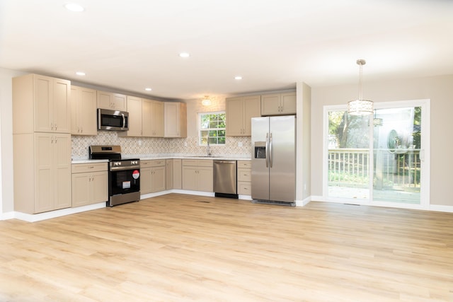 kitchen with backsplash, sink, light hardwood / wood-style flooring, decorative light fixtures, and stainless steel appliances