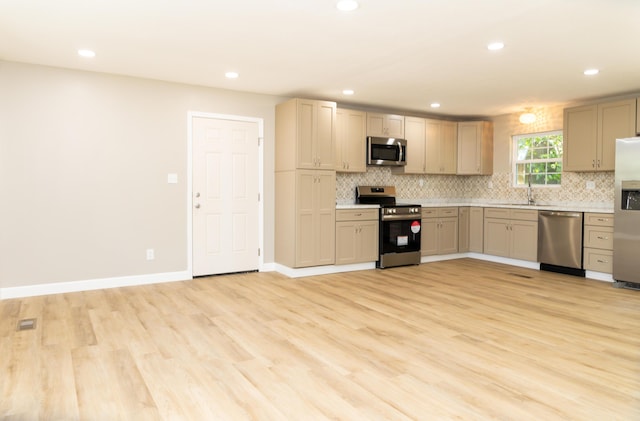 kitchen featuring light brown cabinets, backsplash, sink, light hardwood / wood-style flooring, and appliances with stainless steel finishes