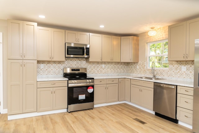 kitchen with sink, light hardwood / wood-style flooring, decorative backsplash, appliances with stainless steel finishes, and cream cabinetry