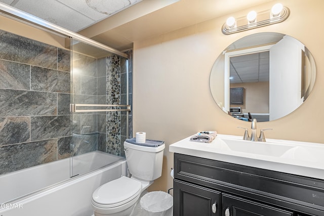 full bathroom featuring vanity, combined bath / shower with glass door, toilet, and a drop ceiling