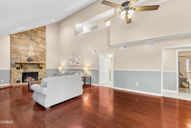 living room featuring wood-type flooring, a stone fireplace, lofted ceiling, and ceiling fan