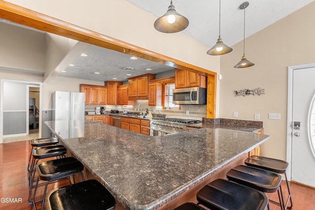 kitchen featuring pendant lighting, appliances with stainless steel finishes, a kitchen breakfast bar, and kitchen peninsula