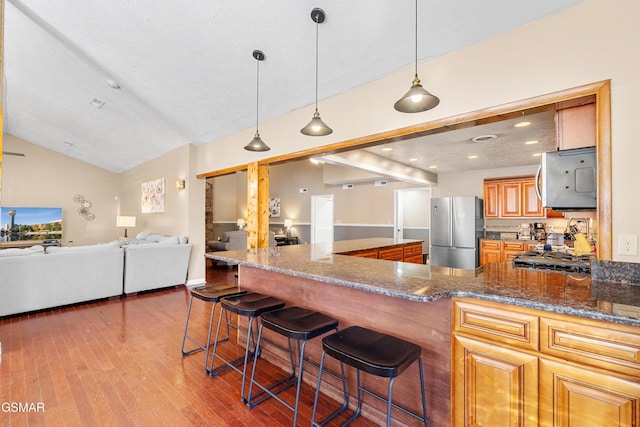 kitchen featuring hanging light fixtures, stainless steel refrigerator, dark stone counters, and a kitchen bar