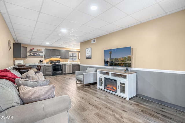 living room with sink, a drop ceiling, and light hardwood / wood-style flooring