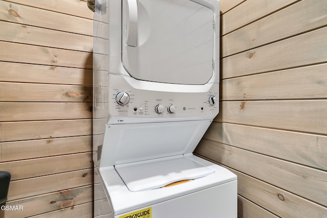 laundry area featuring stacked washer / drying machine and wood walls