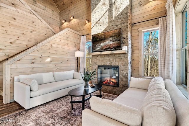 living room with high vaulted ceiling, a stone fireplace, and wooden walls