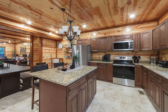 kitchen featuring pendant lighting, a center island, appliances with stainless steel finishes, log walls, and a notable chandelier