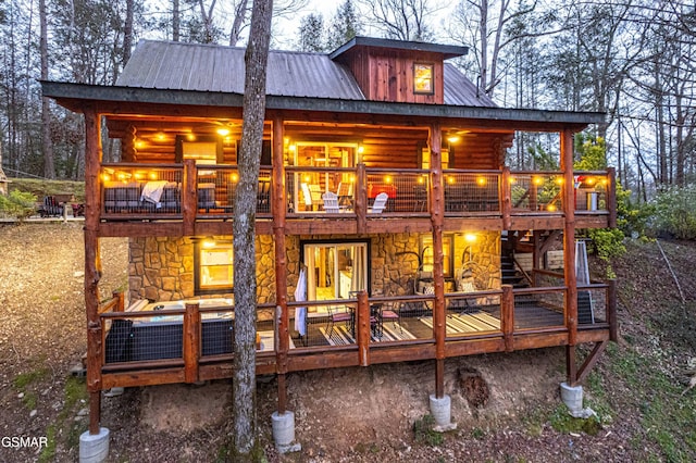 rear view of house with a balcony, stone siding, and metal roof