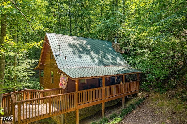 exterior space featuring metal roof, a chimney, a deck, and a view of trees