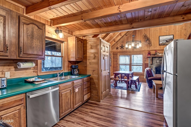 kitchen with appliances with stainless steel finishes, a healthy amount of sunlight, a sink, and wood walls