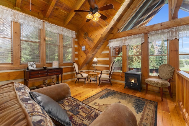 living area with a wood stove, wooden walls, ceiling fan, light wood-type flooring, and beam ceiling