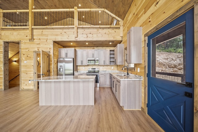 kitchen featuring stainless steel appliances, wooden walls, sink, light hardwood / wood-style floors, and a kitchen island