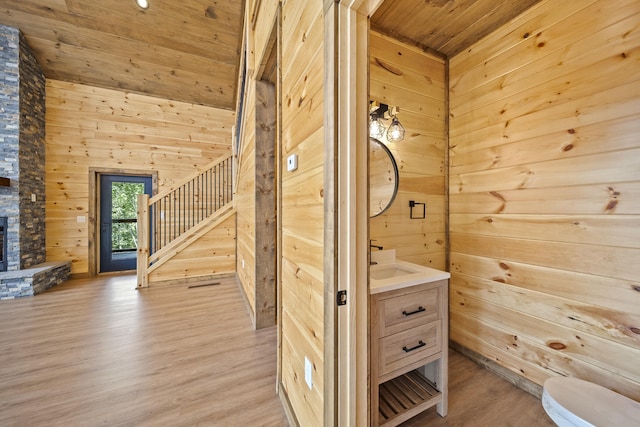 bathroom featuring wood ceiling, vanity, hardwood / wood-style flooring, a fireplace, and wood walls