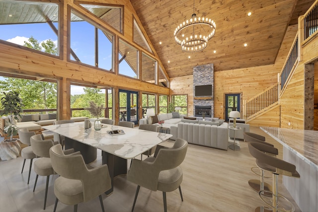 dining space featuring a notable chandelier, a stone fireplace, wooden ceiling, and high vaulted ceiling