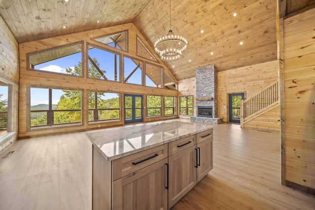 kitchen featuring a kitchen island, a stone fireplace, light stone countertops, and high vaulted ceiling