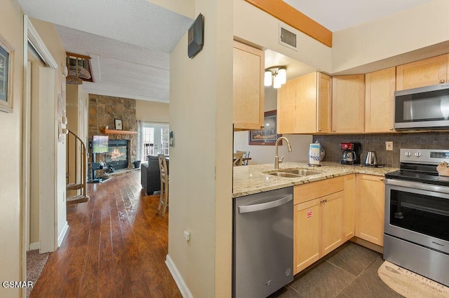 kitchen featuring light stone countertops, appliances with stainless steel finishes, sink, light brown cabinets, and a fireplace