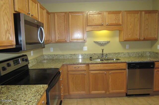 kitchen featuring light stone countertops, sink, light tile patterned flooring, and stainless steel appliances