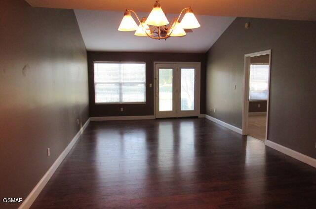 spare room featuring dark wood-type flooring, vaulted ceiling, and an inviting chandelier