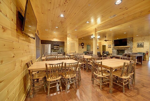 dining room featuring a fireplace, wooden walls, hardwood / wood-style flooring, and wooden ceiling