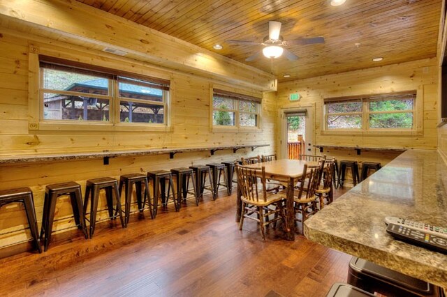 dining area with dark hardwood / wood-style flooring, wood ceiling, ceiling fan, and wood walls