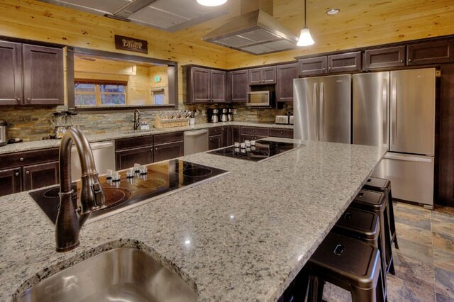 kitchen featuring light stone countertops, decorative light fixtures, range hood, and appliances with stainless steel finishes