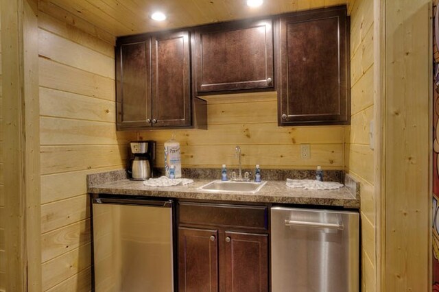 kitchen featuring wood walls, dishwasher, dark brown cabinets, and sink